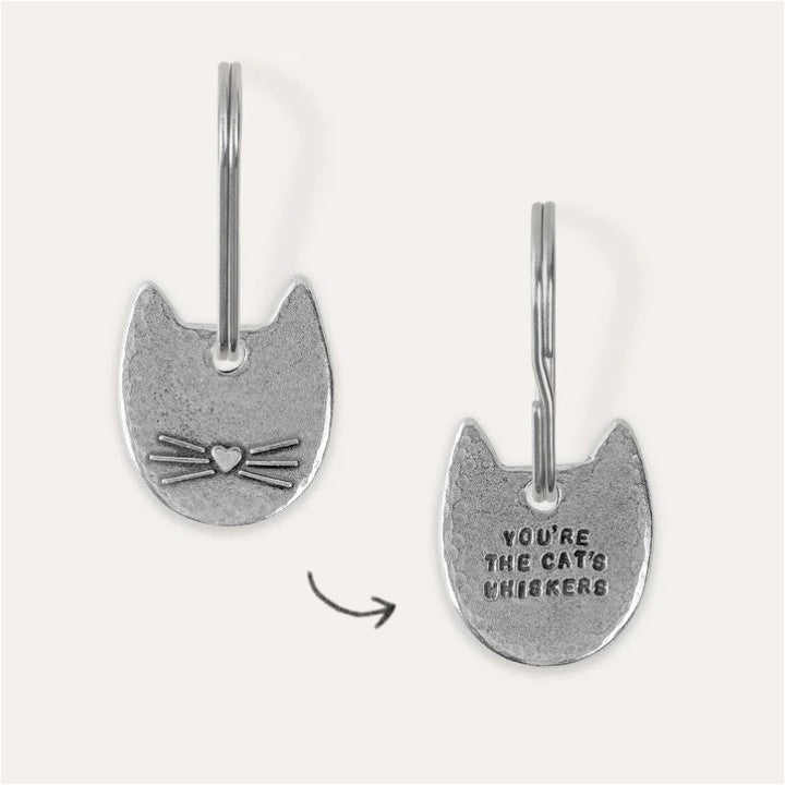 A cat-shaped pewter keychain with embossed and engraved text details, showing front and back designs.