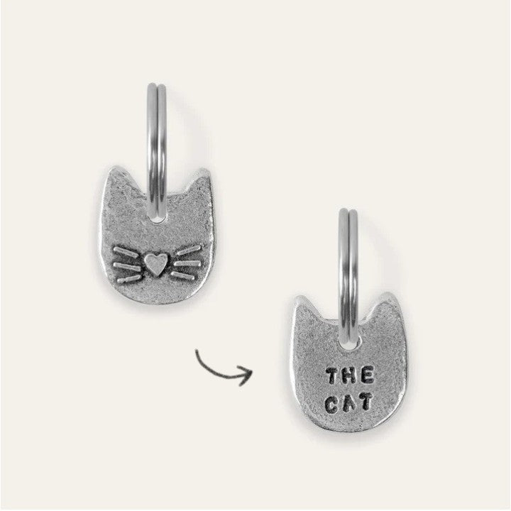 A cat-shaped pewter charm with embossed and engraved text details, showing front and back designs.