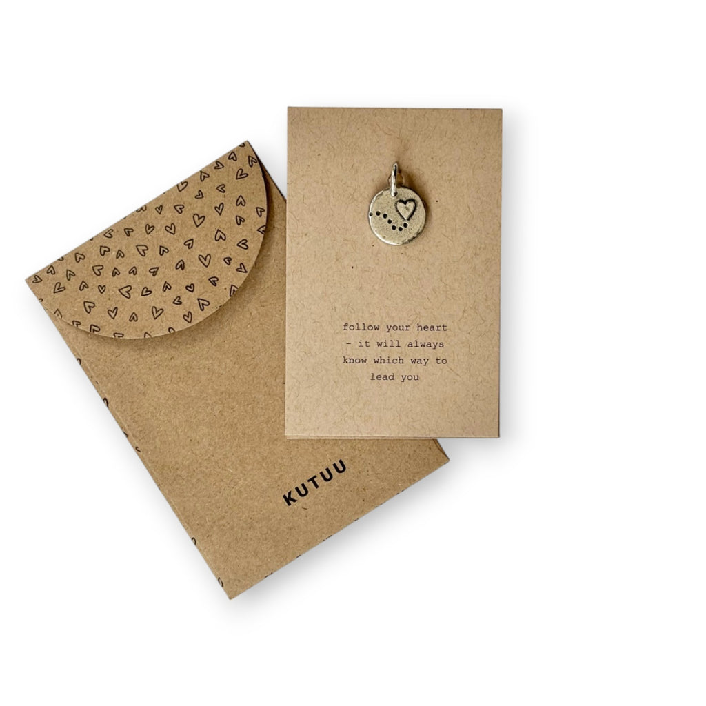 A kraft paper card with heart and dots embossed pewter charm and envelope with hearts-patterned and brand name "KUTUU".