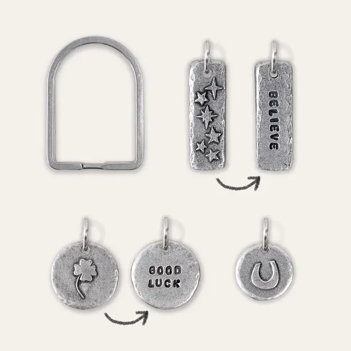 An arch-shaped keyring with three pewter charms in various designs, a horseshoe, a stars "BELIEVE" and a four leaf clover "GOOD LUCK" showing front and back designs.