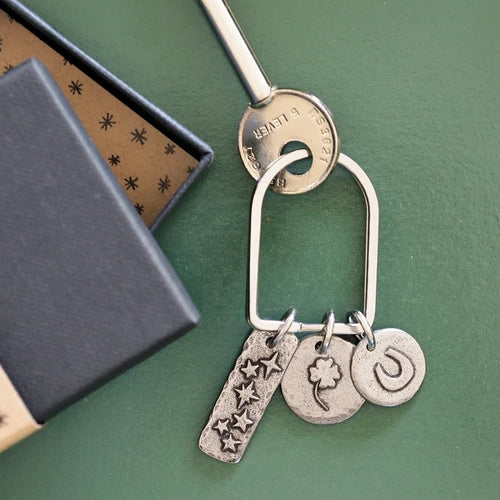 A silver key and a keyring with three pewter charms on a green surface next to a black gift box.