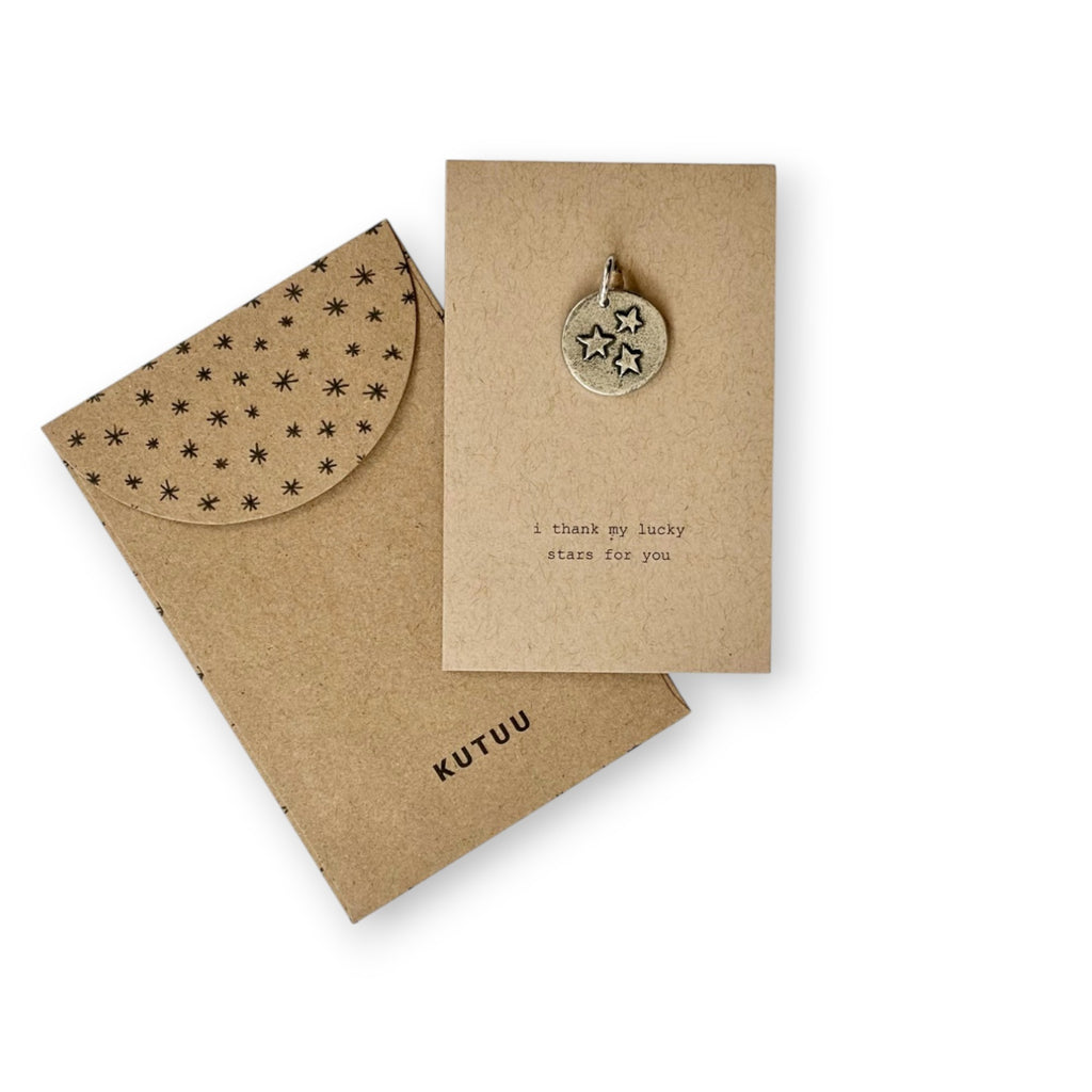 A kraft paper card with stars embossed pewter charm and envelope with star-patterned and brand name "KUTUU".
