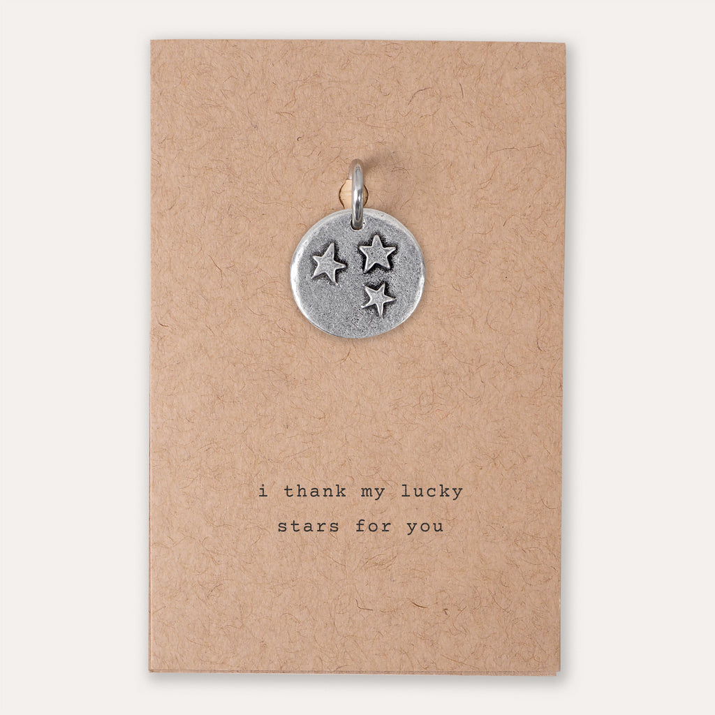 A stars embossed pewter charm on a kraft paper card with the text "i thank my lucky stars for you".