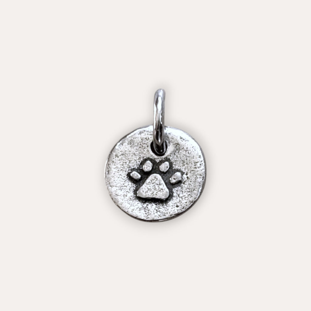A round silver metal charm with an embossed paw print design and a loop at the top.