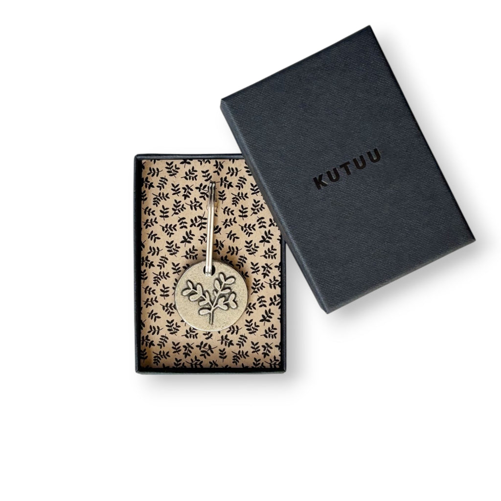 Gift box with a leaf design round pewter keychains on a leaves-patterned lining, with "KUTUU" printed on the lid.
