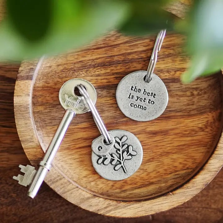 A wooden tray with a key and two round pewter keychains, one with text and the other with a leaf design.
