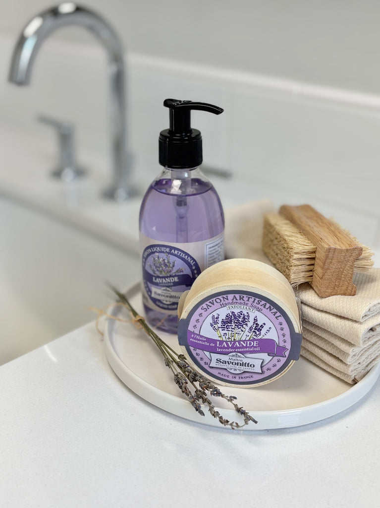 A bathroom countertop featuring lavender soap, folded towels, a brush, and lavender sprigs.