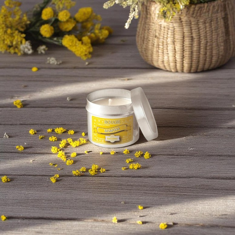 Maitre Savonitto Mimosa Candle in aluminum tin surrounded by yellow mimosa flowers on a gray wooden surface.
