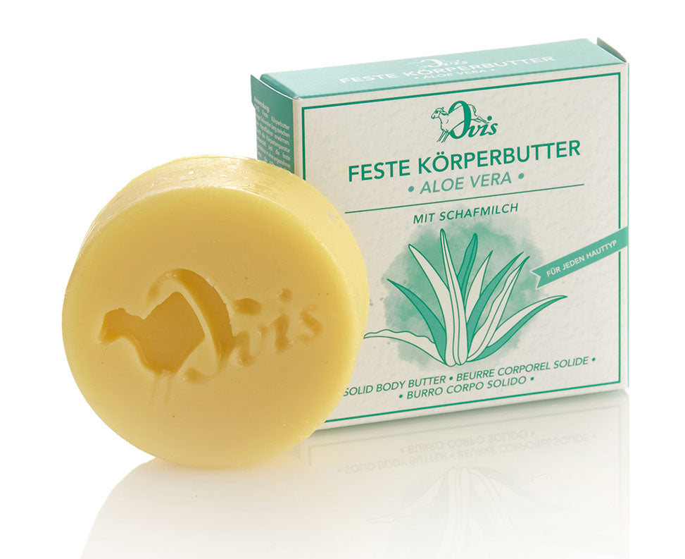 A round pale yellow bar of body butter with embossed design, in front of a green and white box featuring aloe vera illustrations.