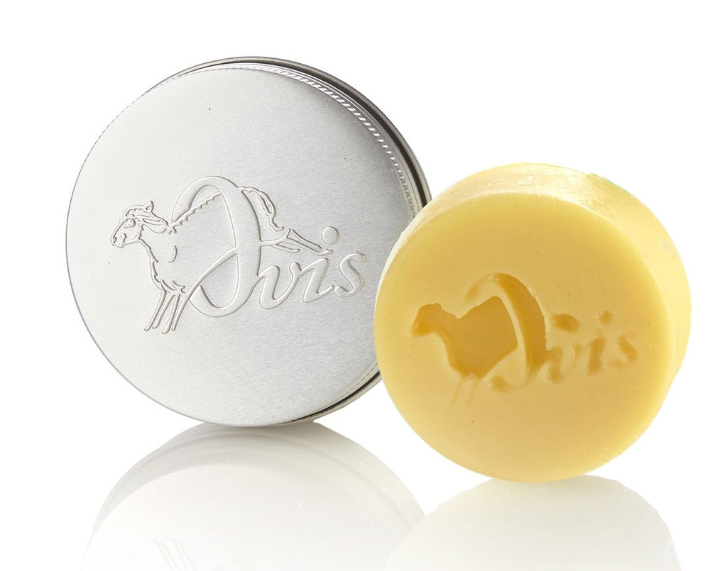 A round, silver tin and a pale yellow body butter bar, both embossed with a sheep and the word "Ovis."