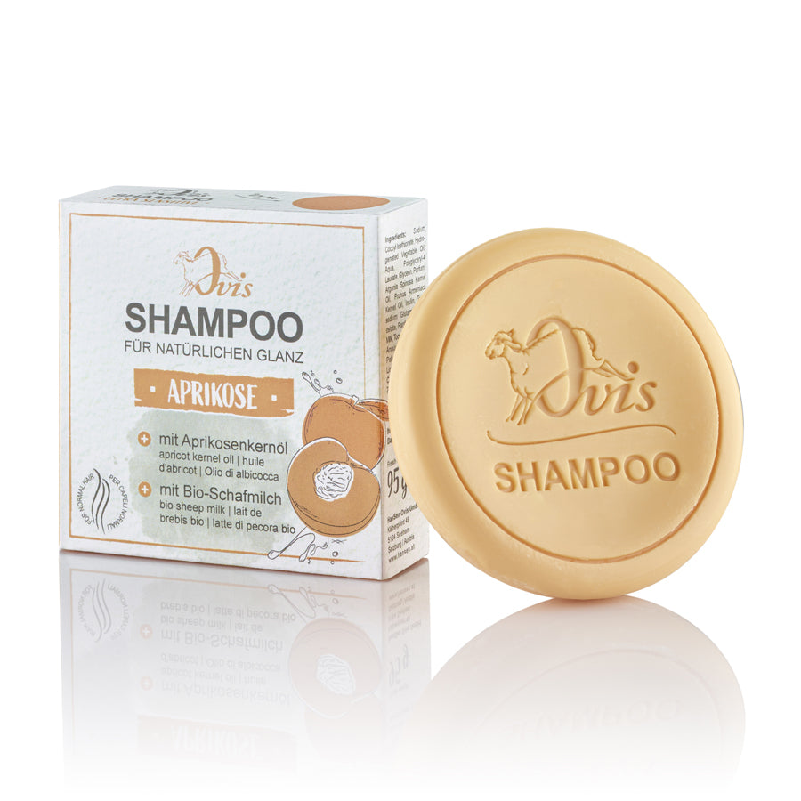 Round beige shampoo bar and its cardboard packaging with apricot illustrations.