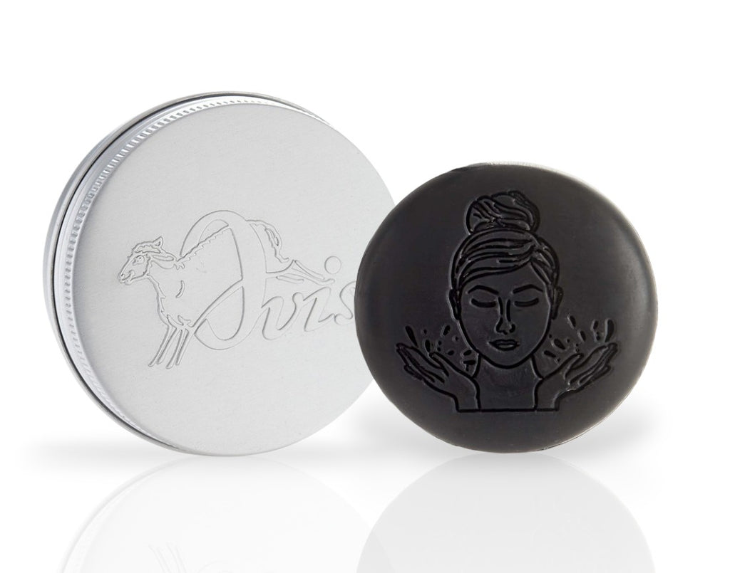 Round black facial soap with embossed face design, and a silver travel tin with sheep illustration and "Ovis" text.