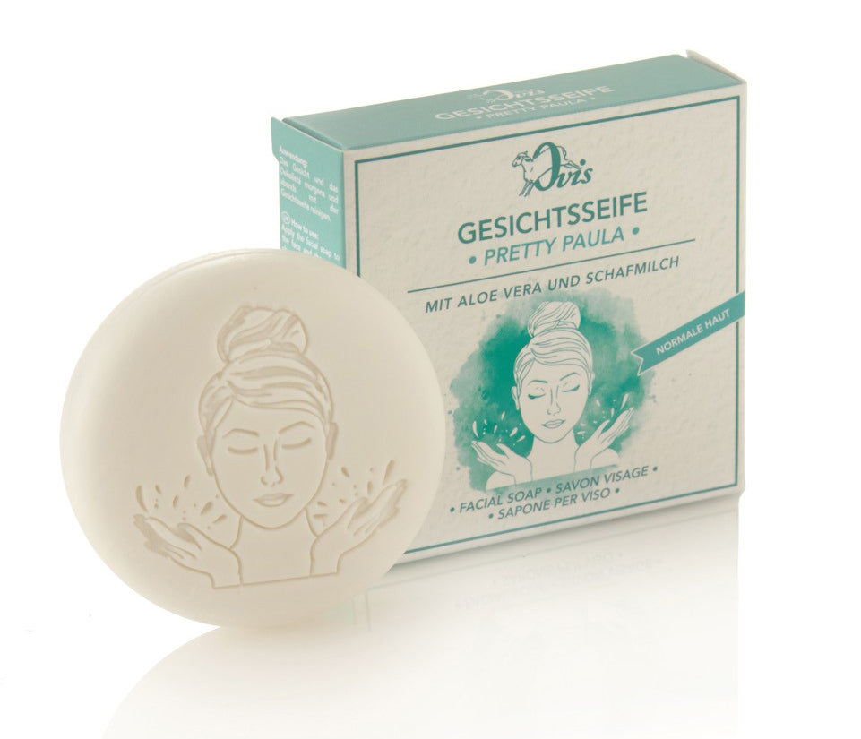 Round white facial soap with an embossed woman's face, positioned in front of a green and white box with matching illustration.