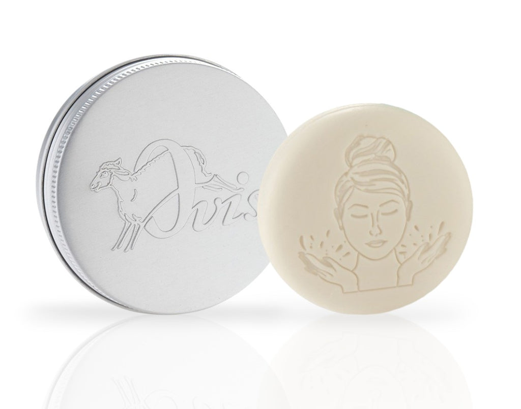 Round white facial soap with embossed face design, and a silver travel tin with sheep illustration and "Ovis" text.
