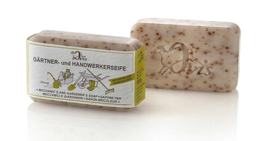 Two beige speckled soap bars, one wrapped with a gardening-themed label and the other embossed with a sheep logo.