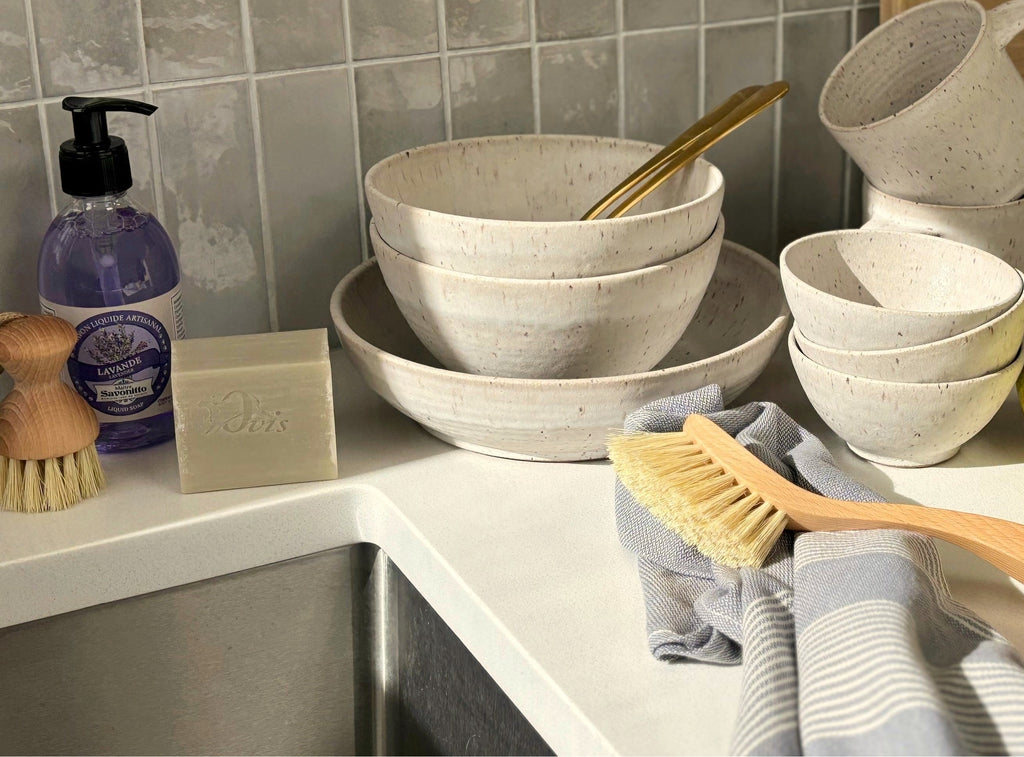 A kitchen counter with stacked ceramic bowls, soap, and cleaning brushes.