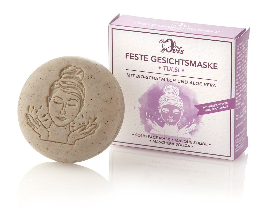 Round beige solid facial mask with an embossed woman's face, positioned in front of a purple and white box with matching illustration.