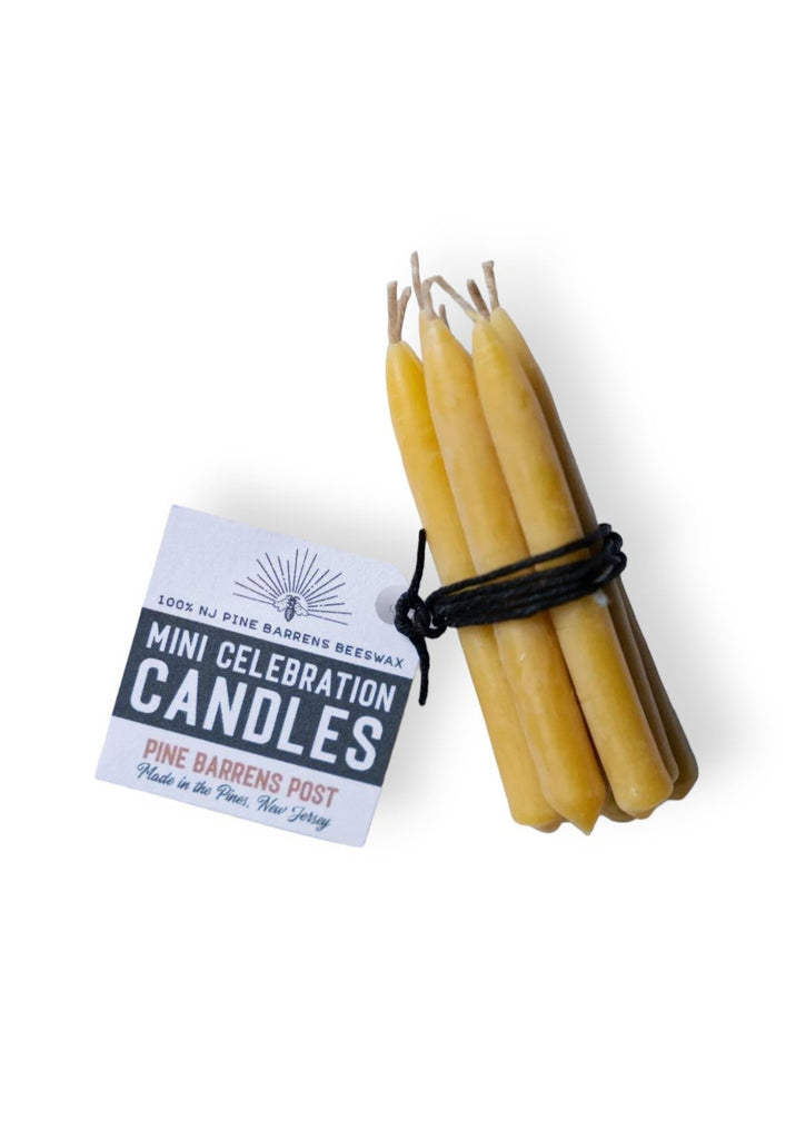 A set of eight small beeswax candles tied with black string, with a white label attached with brand name "Pine Barrens Post" and illustration.