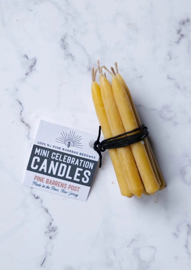 A set of eight small beeswax candles tied with black string, with a white label attached with brand name "Pine Barrens Post" and illustration.