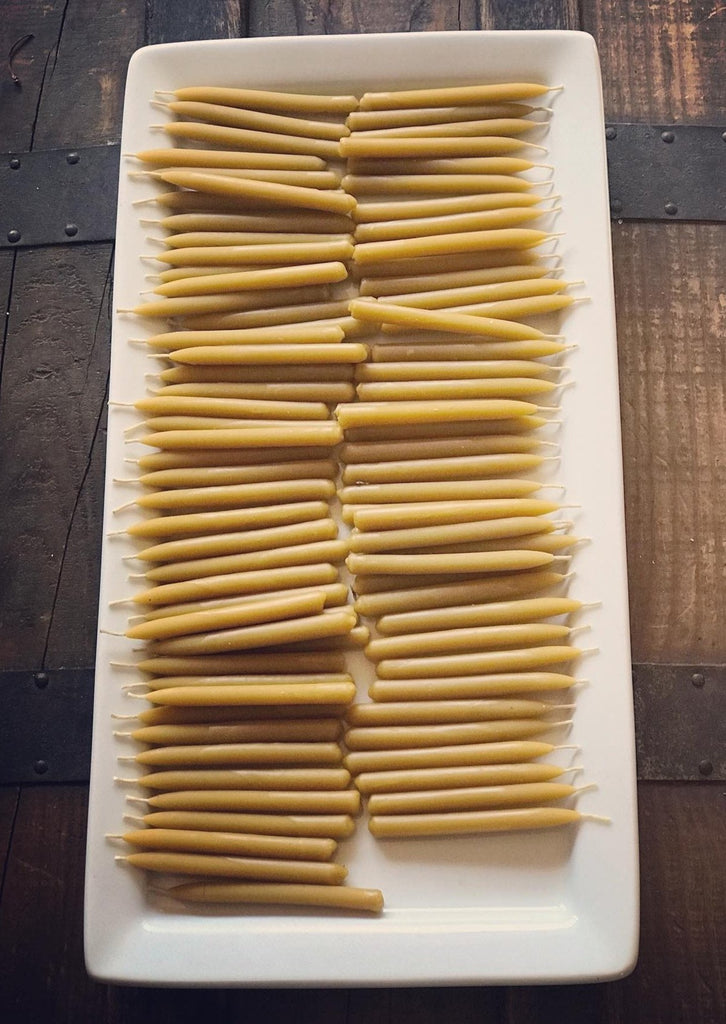 A white platter filled with small beeswax candles arranged on a wooden table.