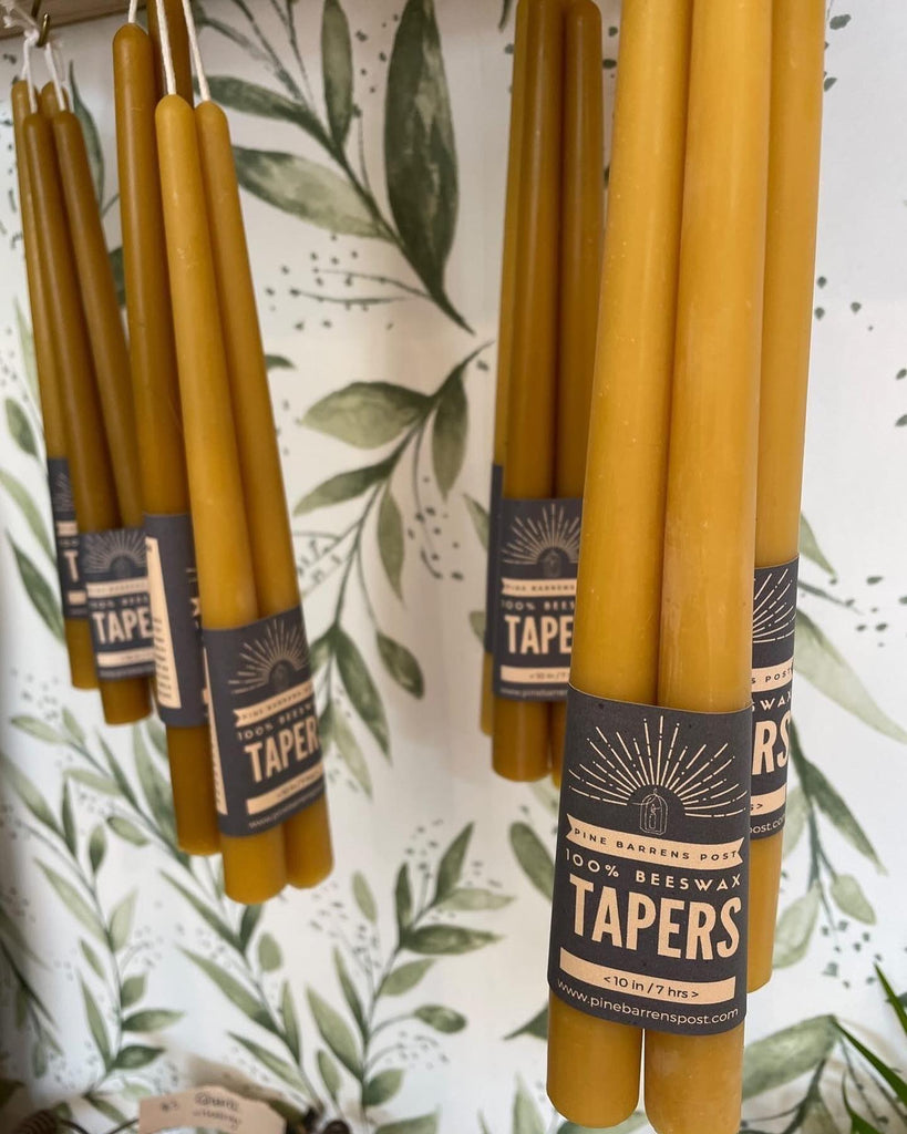"Pine Barrens Post" taper candles hanging against a leafy wallpaper background.