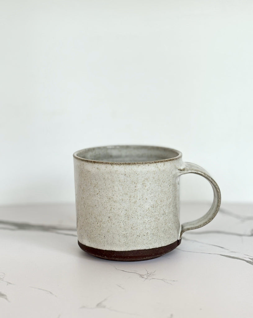 A gray speckled ceramic mug with dark brown coating on the bottom on a marbled surface.