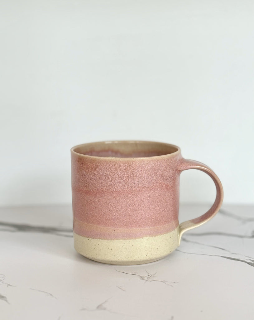 A pink and beige two-toned gradient color ceramic mug on a marbled surface.