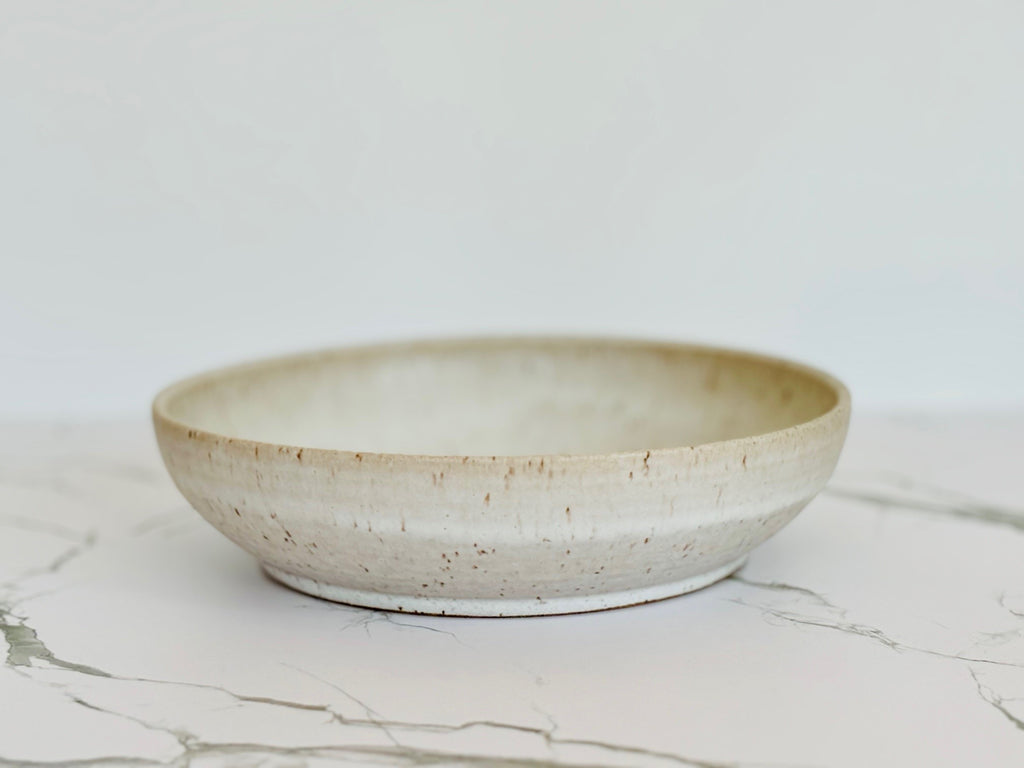 A beige speckled ceramic pasta bowl on a marbled surface.