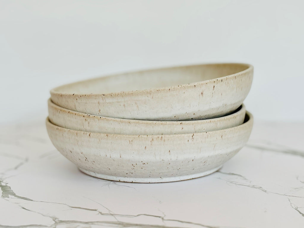 A stack of beige speckled ceramic pasta bowl on a marbled surface.