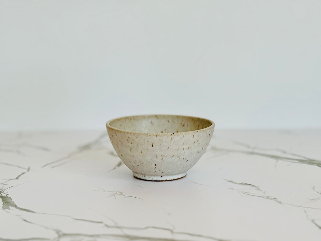 A small beige speckled ceramic bowl on a marbled surface.