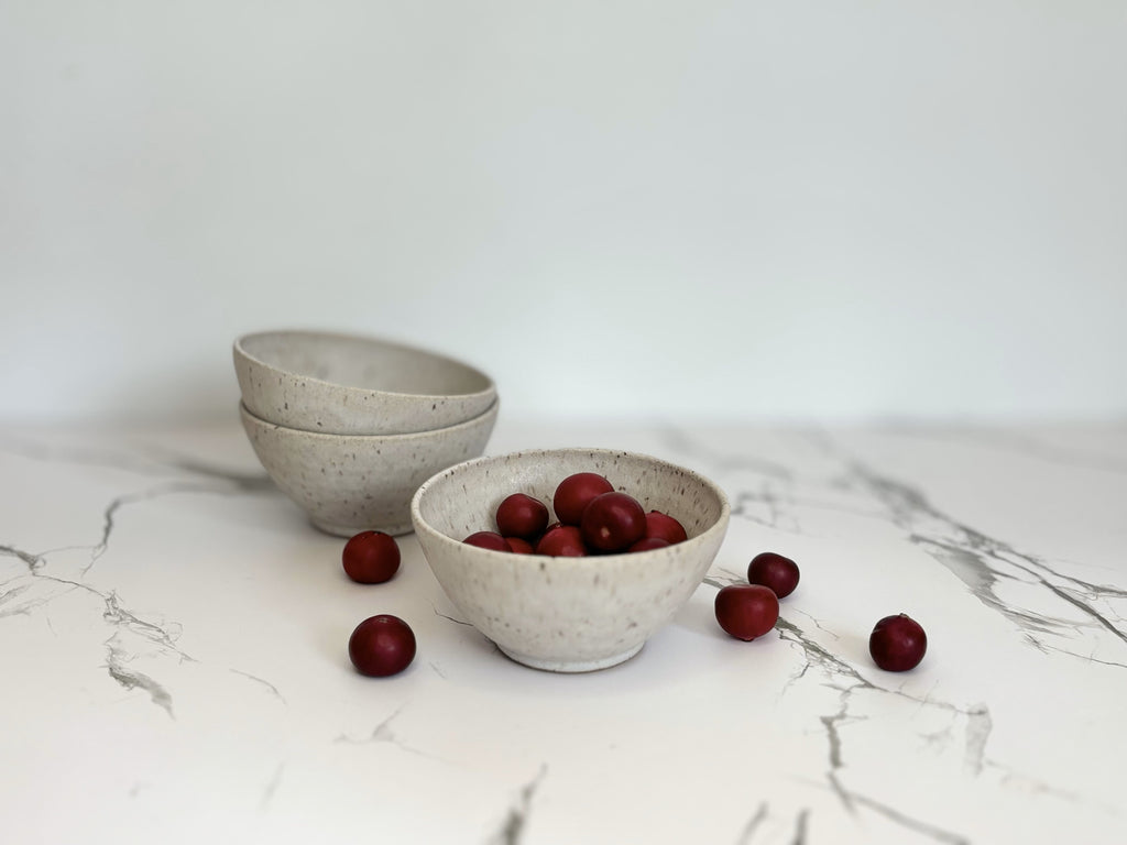 Three small beige speckled ceramic bowls on a marbled surface with cranberries.