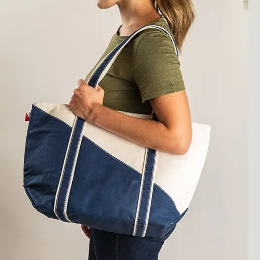 A person holding a ShoreBags Contemporary Canvas Tote bag with off-white and navy blue diagonal design and navy blue handles.