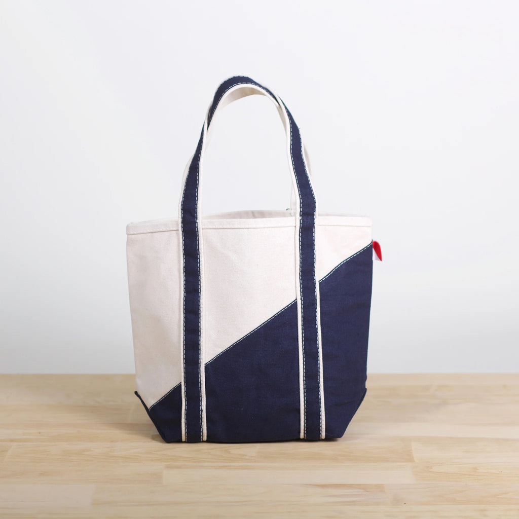 ShoreBags Mini Contemporary Canvas Tote bag with off-white and navy blue diagonal design and navy blue handles on a light wooden surface.