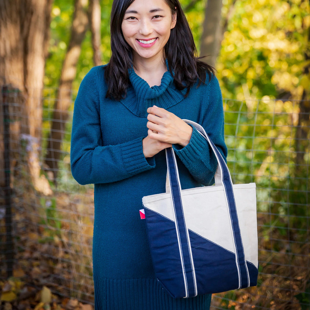 Person in a teal sweater holding a two-toned ShoreBags Mini Contemporary Canvas Tote bag with trees and foliage in the background.