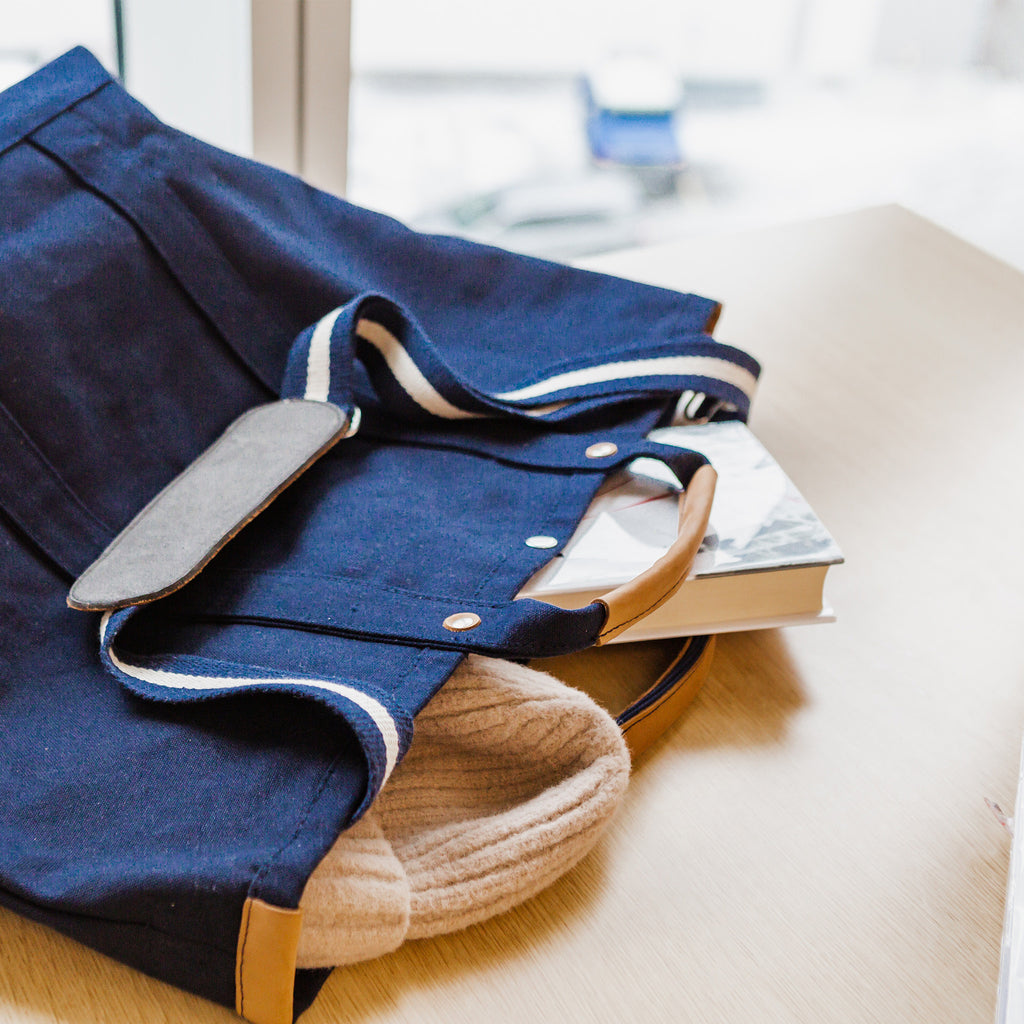 ShoreBags Navy Cargo Canvas Travel Tote bag with a cream sweater and a book on a wooden table.
