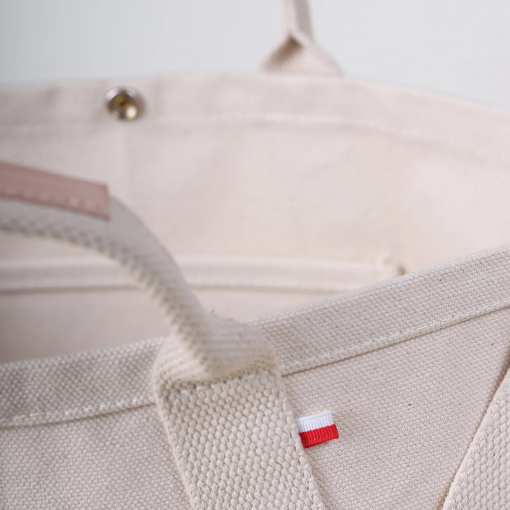 Close-up of ShoreBags Utility Heavyweight Canvas Tote bag with a red and white tag and a metal snap button.