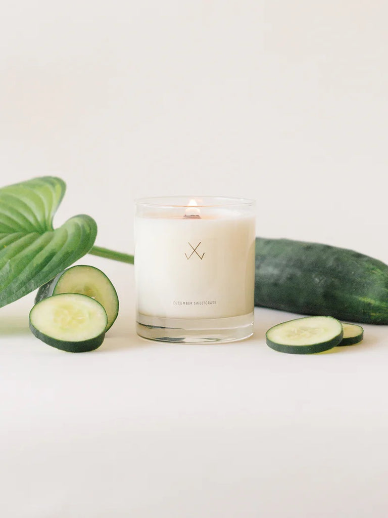A Simply Curated cucumber sweetgrass soy candle with cucumber slices and a large green leaf on the side.