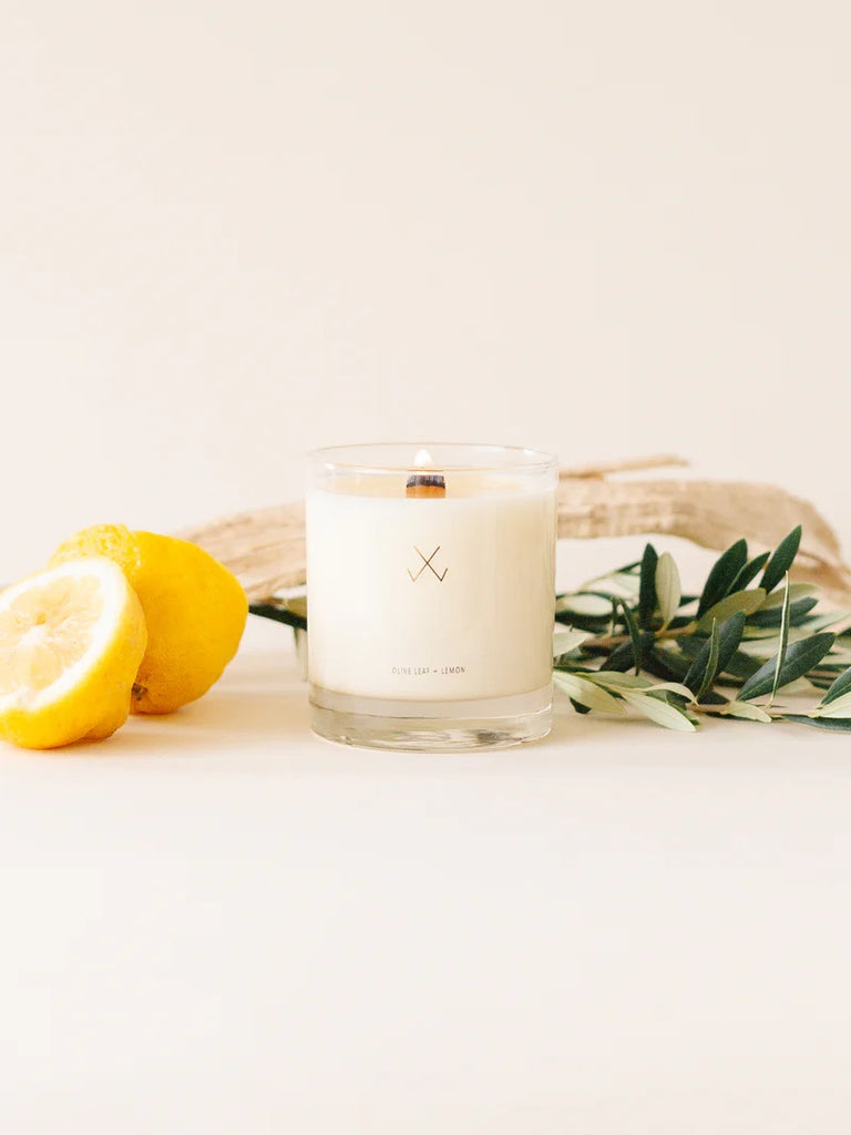 A Simply Curated olive leaf + lemon soy candle with lemons and olive leaves on the side.