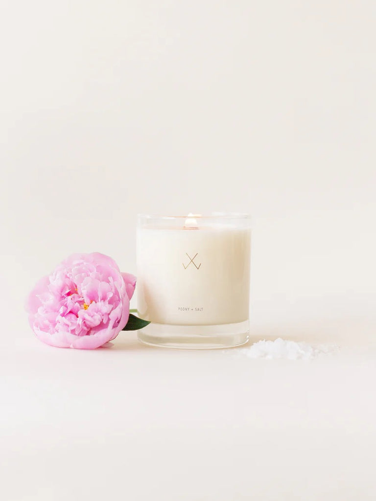 A Simply Curated peony + salt soy candle with a pink peony flower and a pinch of salt.