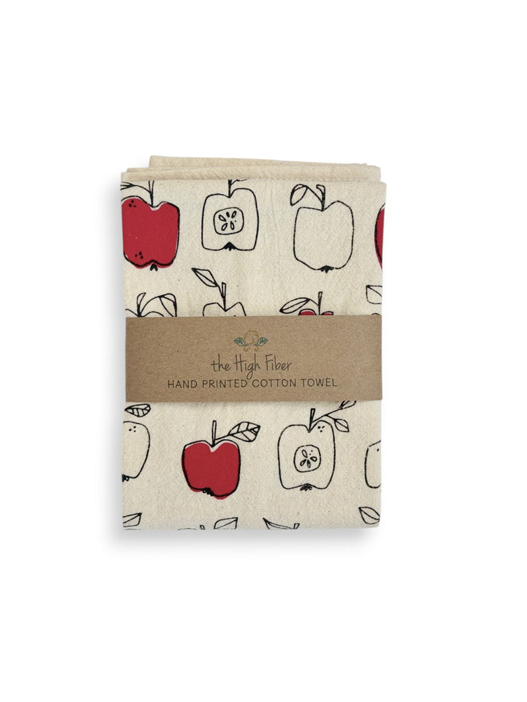 A natural cotton tea towel with red and black-outlined apples print and a brown paper band with brand name "the High Fiber" and logo.