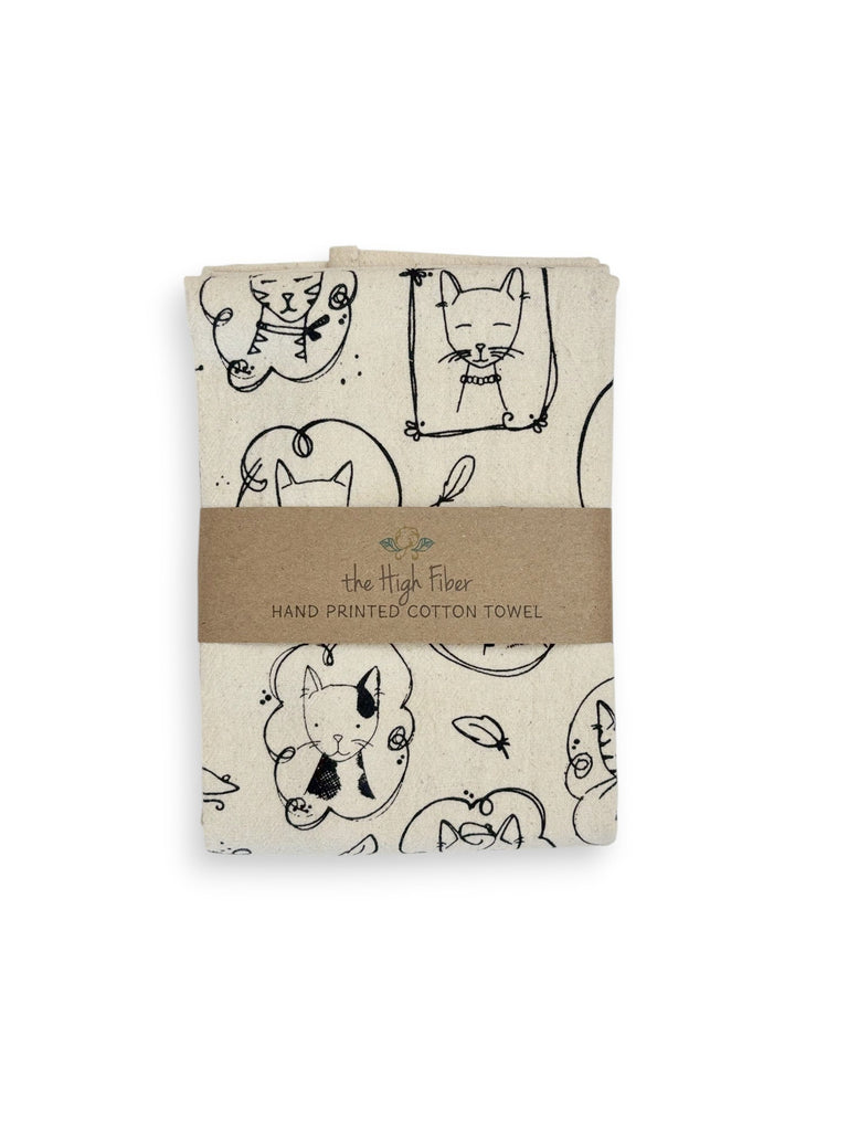 A folded natural cotton tea towel with various cats portrait patterns and a brown paper band with brand name "the High Fiber" and logo.