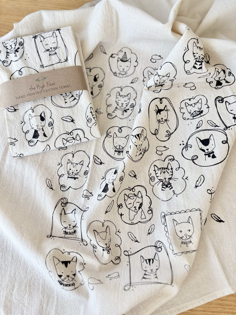 A natural cotton tea towels with various cats portrait patterns, with another tea towel wrapped in a brown paper band with "the High Fiber" and the logo printed on it. 
