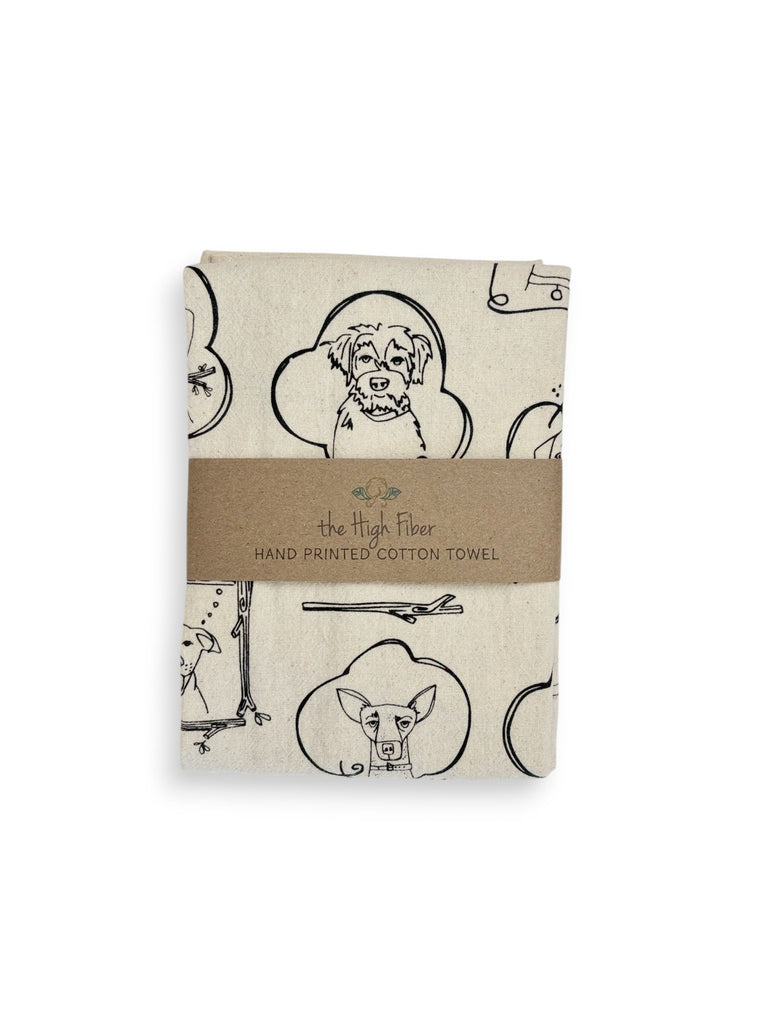 A folded natural cotton tea towel with various dogs portrait patterns and a brown paper band with brand name "the High Fiber" and logo.