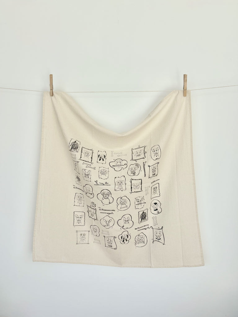A natural cotton tea towel with various dogs portrait patterns hanging on a clothesline. 