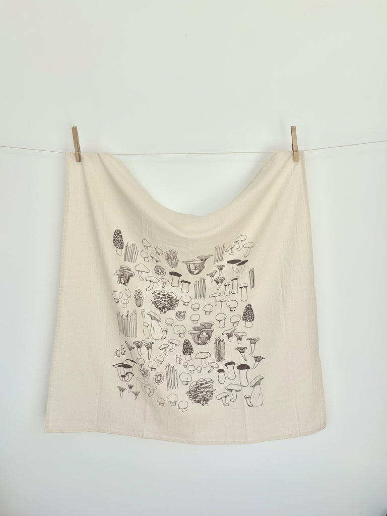 A natural cotton tea towel with taupe mushrooms patterns hanging on a clothesline.