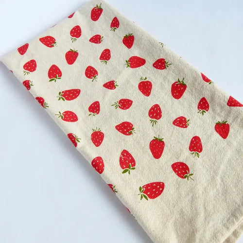 Beige tea towel with red strawberries patterns on an off-white background.