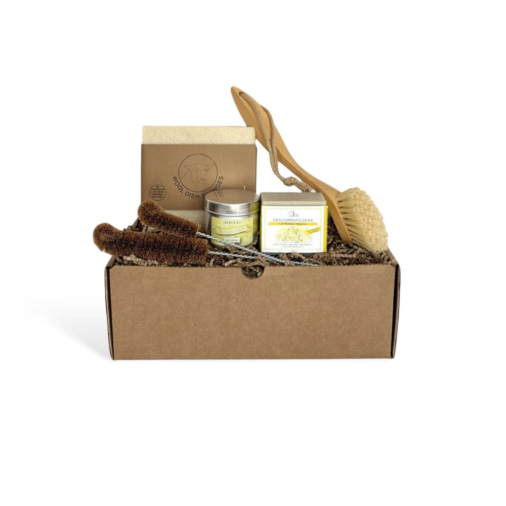 Eco-friendly dish-washing gift box containing a wooden dish brush, a dish soap, a wool sponge, two sizes of bottle brush and and a candle tin.