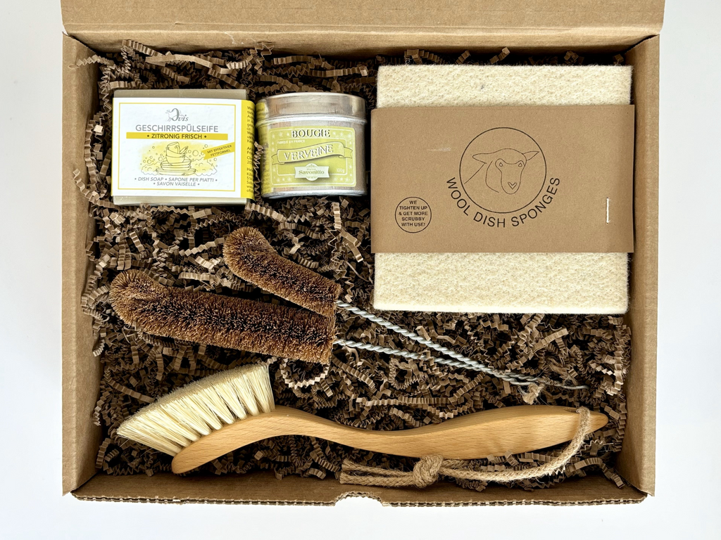 Top view of eco-friendly dish-washing gift box containing a wooden dish brush, a dish soap, a wool sponge, two sizes of bottle brush and and a candle tin.