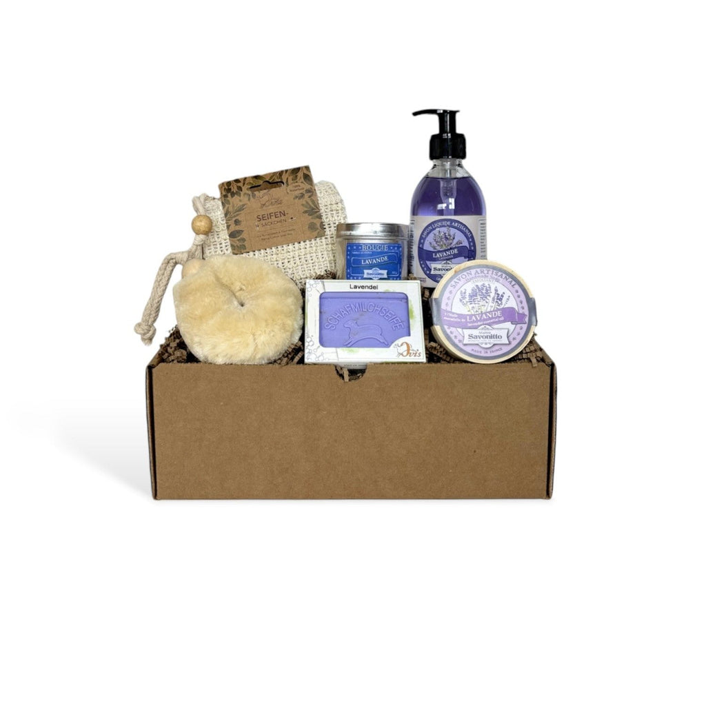 A gift box of lavender bath products including a soap bar, a round soap in wood box, a candle tin, a bottle of liquid soap, a soap bag and a body brush.