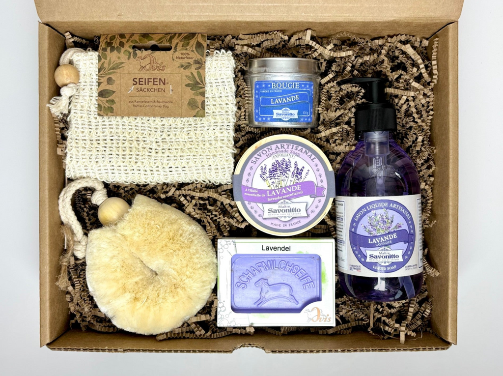 Top view of a gift box of lavender bath products including a soap bar, a round soap in wood box, a candle tin, a bottle of liquid soap, a soap bag and a body brush.